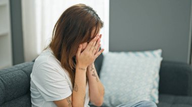 Genç, güzel İspanyol kadın kanepede oturup evde ağlıyor.