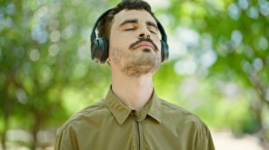 Genç İspanyol adam parkta rahatça müzik dinliyor.