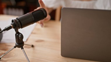 Genç bayan radyo muhabiri radyo stüdyosunda mikrofona dokunuyor.