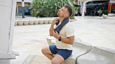 Genç adam parkta bankta otururken terini havluyla siler.