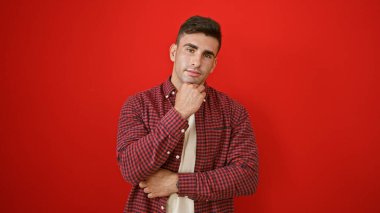 Havalı, çekici İspanyol genç adam canlı kırmızı bir arka planda tek başına dururken ciddi bir ifade takınıyor. Rahat bir yaşam tarzı yakalayan bir portre.