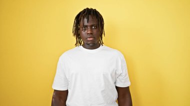 İzole edilmiş sarı arka plan üzerinde ciddi bir ifadeyle duran Afrikalı Amerikalı adam.