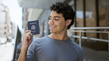 Amerika Birleşik Devletleri pasaportu elinde tutarak gülümseyen genç Latin adam.