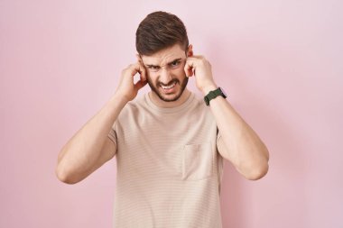Pembe arka planda duran İspanyol sakallı adam yüksek sesli müzik sesi için kulaklarını parmaklarıyla kapatıyor. sağır kavramı. 