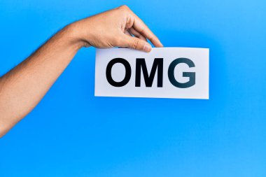 Hand of caucasian man holding paper with omg word over isolated blue background