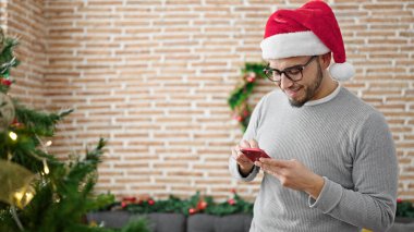 Evde akıllı telefon kullanan İspanyol adam Noel şapkası takıyor.