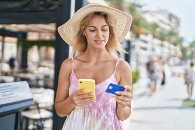 Kafe terasında akıllı telefon ve kredi kartı kullanan genç sarışın kadın turist.