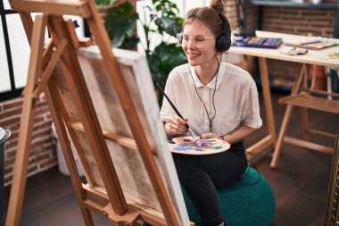 Sanat stüdyosunda müzik dinleyen genç sarışın kadın sanatçı.