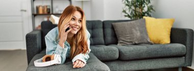 Young caucasian woman talking on the smartphone lying on sofa at home