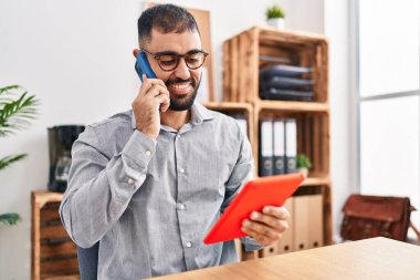 Genç İspanyol iş adamı. Ofiste dokunmatik ped kullanarak akıllı telefondan konuşuyor.