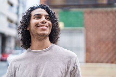 Genç Latin adam gülümsüyor. Kendine güveniyor. Caddenin kenarına bakıyor.