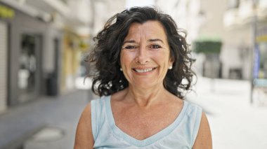 Orta yaşlı İspanyol kadın sokakta kendine güvenerek gülümsüyor.