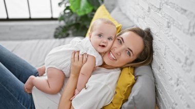 Neşeli anne yatakta uzanıyor, yatak odasında güzel gülümseyen kızına sarılıyor, ev ortamında sevgisini ifade ediyor.