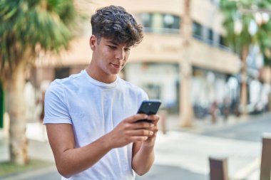 Young hispanic teenager smiling confident using smartphone at street