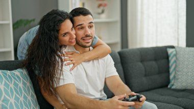 Man and woman couple playing video game sitting on sofa at home