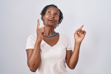 Beyaz arka plan üzerinde duran Afrikalı kadın şaşırdı ve şaşırdı parmaklarıyla işaret etti ve kollarını kaldırdı.. 