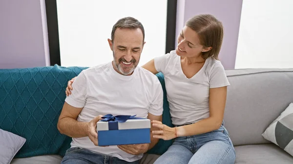 Father\'s loving surprise gift leaves birthday girl, his daughter, smiling and happily surprised on their casual, relaxing living room sofa at home.