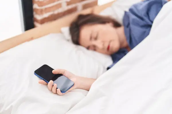 Middle age woman holding smartphone sleeping at bedroom