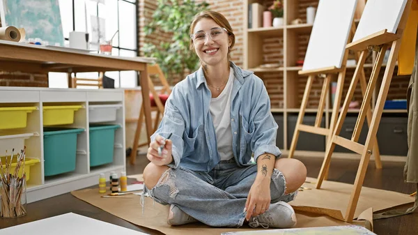年轻的女艺术家坐在地板上 手握画笔 微笑在艺术工作室里 — 图库照片