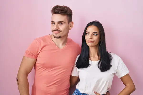 Young Hispanic Couple Standing Pink Background Smiling Looking Side Staring —  Fotos de Stock
