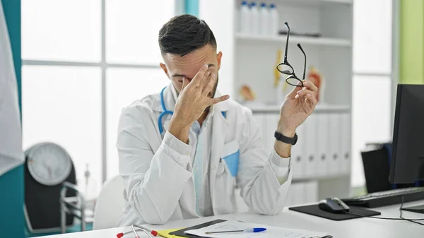 Young hispanic man doctor stressed taking glasses off at the clinic