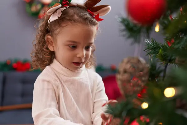 Geyik kulağı takan sevimli sarışın kız evde Noel ağacı süslüyor.