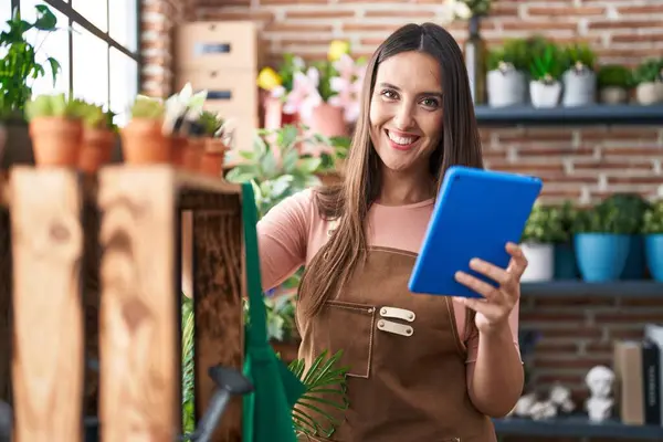 Young beautiful hispanic woman florist smiling confident using touchpad at flower shop