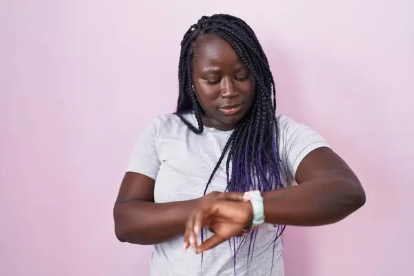 年轻的非洲女人站在粉红的背景上 用腕表检查时间 放松而自信 — 图库照片