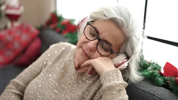 Middle age woman with grey hair sleeping on sofa by christmas tree at home