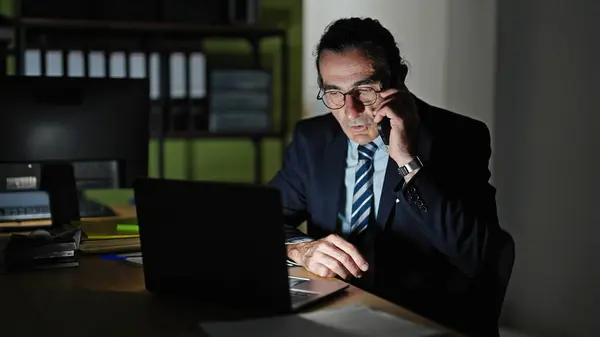 Middle age man business worker using laptop talking on smartphone at the office