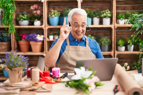 Middle age man with grey hair working at florist shop doing video call smiling with an idea or question pointing finger with happy face, number one