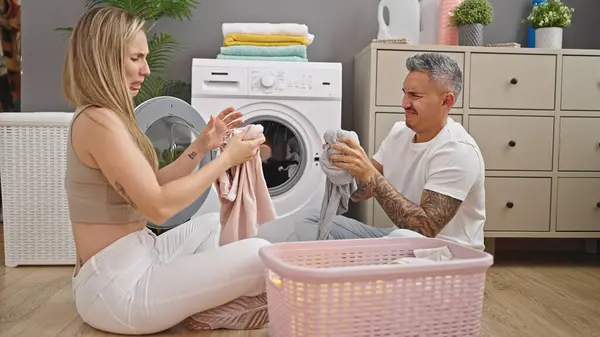 洗濯室で汚れた服を嗅いで床に座っている男女カップル — ストック写真