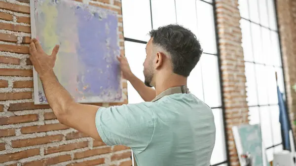 Young arab man artist hanging draw on wall at art studio