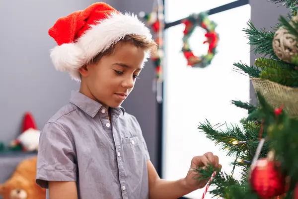 自宅でクリスマスツリーを飾る自信を持って微笑む愛らしいヒスパニックの少年 — ストック写真