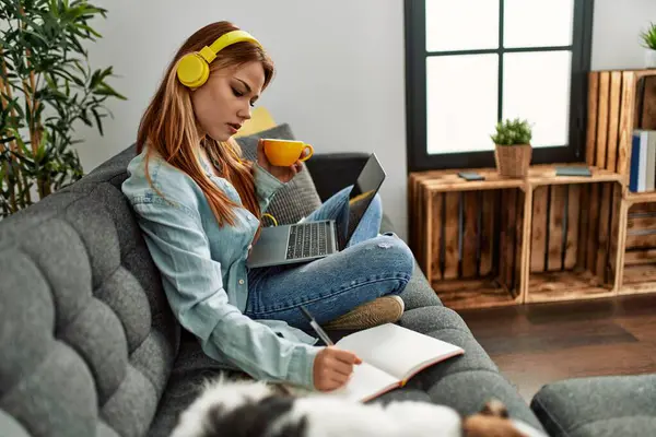 Young caucasian woman sitting on sofa with dog studying at home