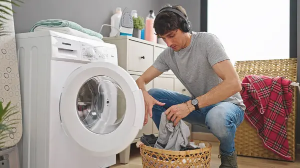 Young hispanic man washing clothes listening to music at laundry room