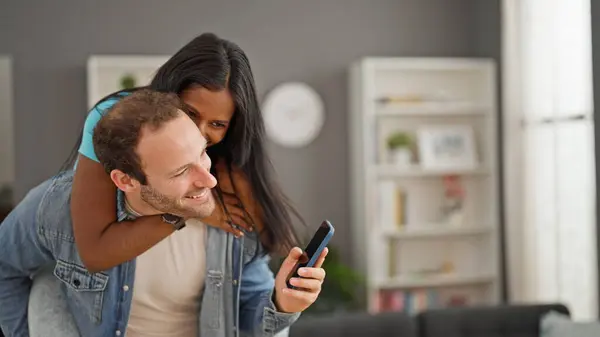 自宅で笑顔でガールフレンドとスマートフォンを保持する美しいカップル — ストック写真