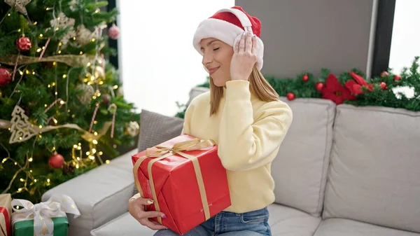 自宅でクリスマスツリーで贈り物を保持する音楽を聴く若い金髪の女性 — ストック写真