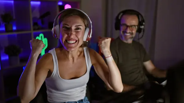 Exciting night in gaming room, two cheerful gamers, father and daughter, triumph together in epic video game win, streaming their victory with headsets and smiles