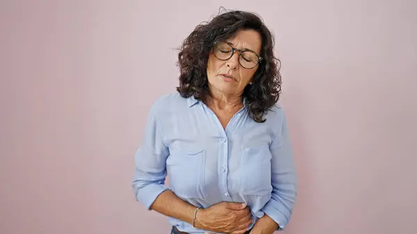 Middle age hispanic woman suffering for stomach ache standing over isolated pink background