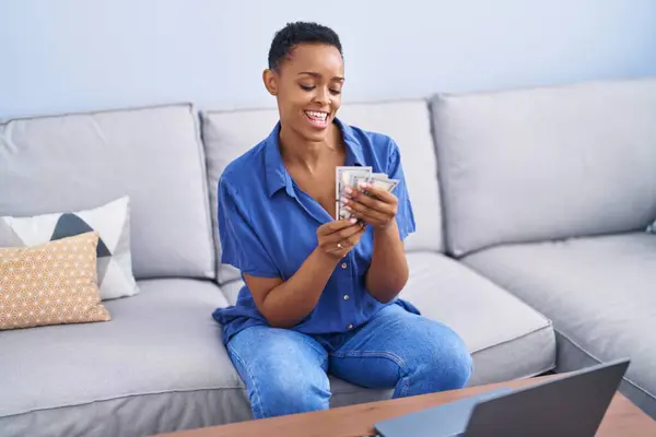 African american woman counting dollars sitting on sofa at home