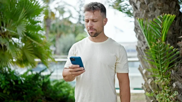 stock image Young man using smartphone with serious expression at park