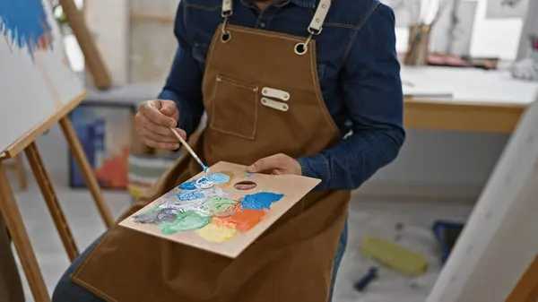 Bearded young hispanic artist painting with passion, drawing lesson in studio, enthusiastically embracing artistic creativity with brush, canvas and colour palette
