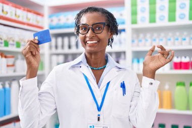 Eczanede çalışan Afrikalı bir kadın elinde kredi kartıyla mutlu bir şekilde gülümsüyor. 