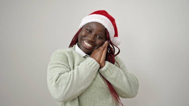 Saçları örgülü, gülümseyen, kendine güvenen, beyaz arka planda Noel şapkası takan Afrikalı bir kadın.