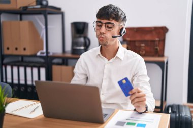 Bilgisayarda çalışan genç İspanyol adam elinde kredi kartıyla kameraya bakıyor ve canlı yayında öpüşüyor. Sevimli ve seksi. aşk ifadesi. 