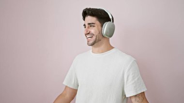 Akıllı telefon ve kulaklık kullanan genç İspanyol adam izole edilmiş pembe arka planda müzik dinliyor.