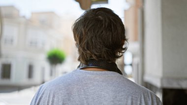 Serin, sakallı genç adam güneşli bir caddede, kulaklık takmış, kentsel yaşam tarzını özümsüyor..