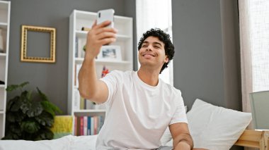 Genç latin adam yatak odasındaki yatakta video görüşmesi yapıyor.