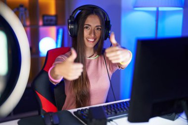 Video oyunları oynayan genç İspanyol kadın elleriyle olumlu jest yapmayı onaylıyor, gülümsüyor ve başarı için seviniyor. kazanan jest. 